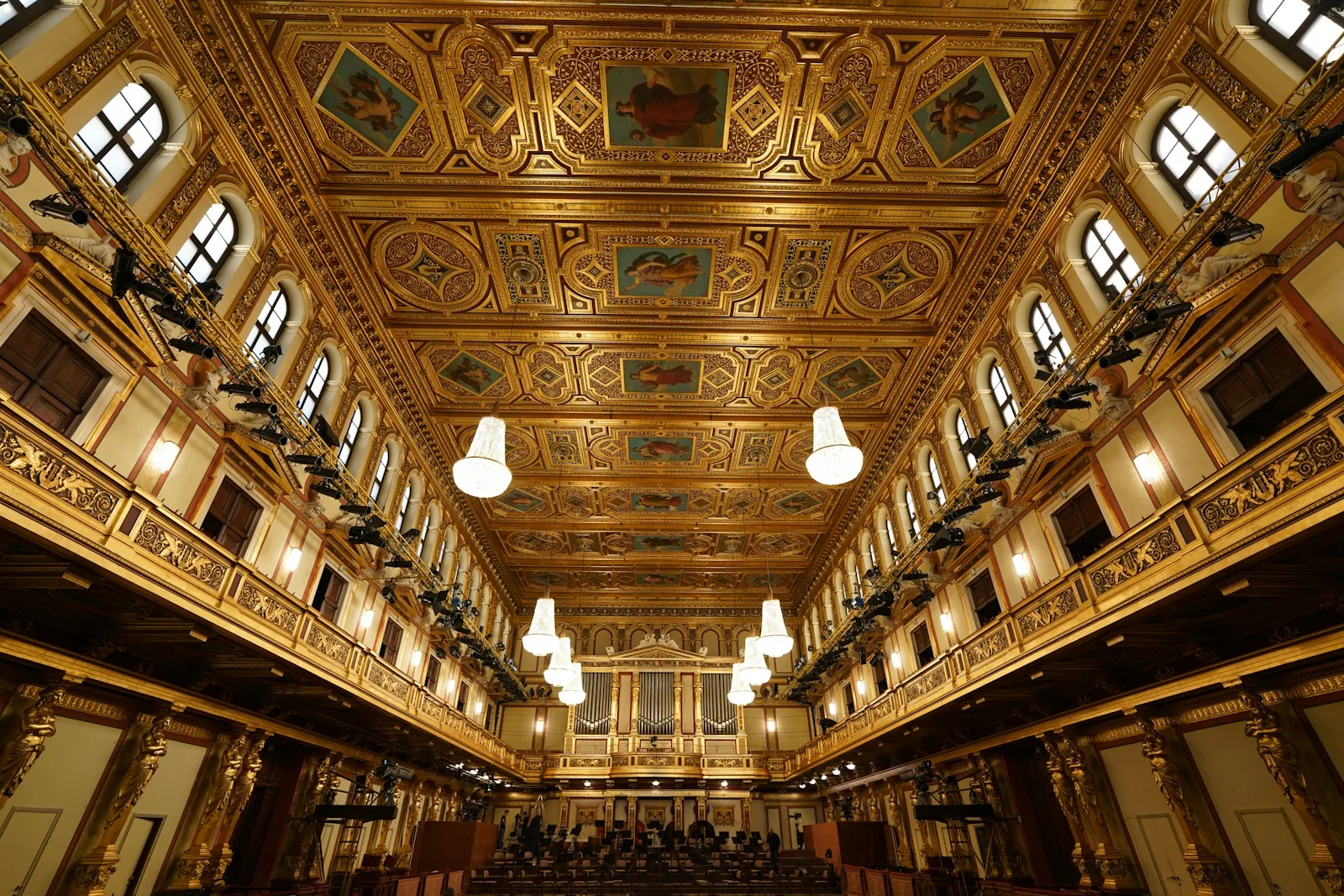 The gilded interior of a concert hall with chandeliers and a pipe organ.